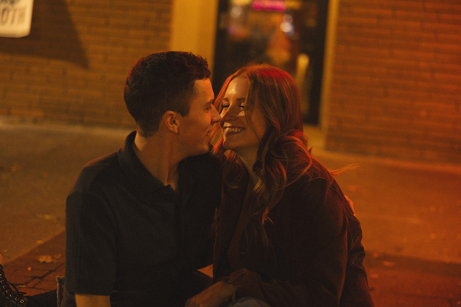 Candid photo of a woman laughing with her fiancé during their night time Michigan engagement photos outside of a bar.