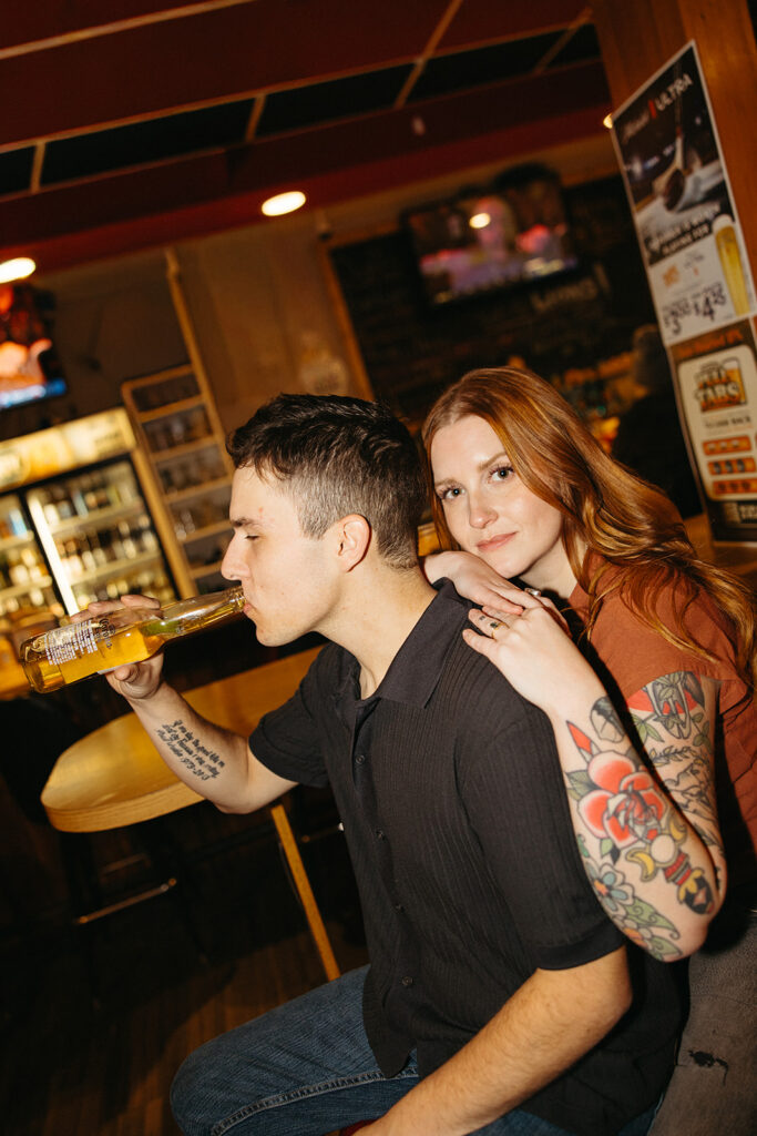 Man drinking a beer while his fiancé leans on his back at The Evening Post Bar & Grill in Clare, Michigan.
