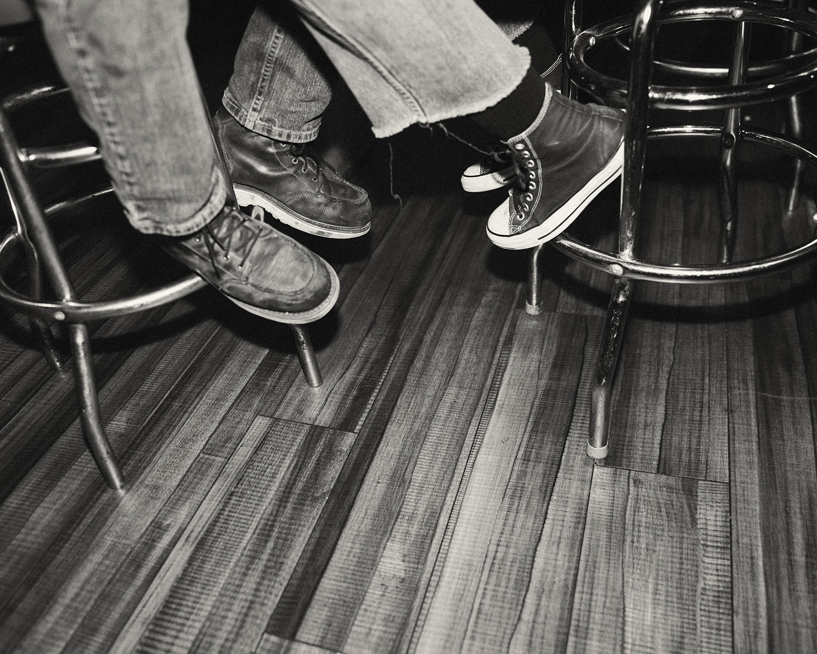 Black and white photo of a couple sitting on barstools just showing their shoes.