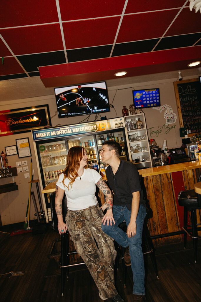 Couple sitting at the bar and laughing for their Michigan engagement photos at The Evening Post Bar & Grill in Clare, Michigan.