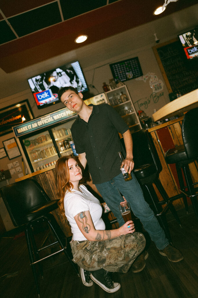 Couple posing in front of the bar at The Evening Post Bar & Grill in Clare, Michigan for dive bar engagement photos.