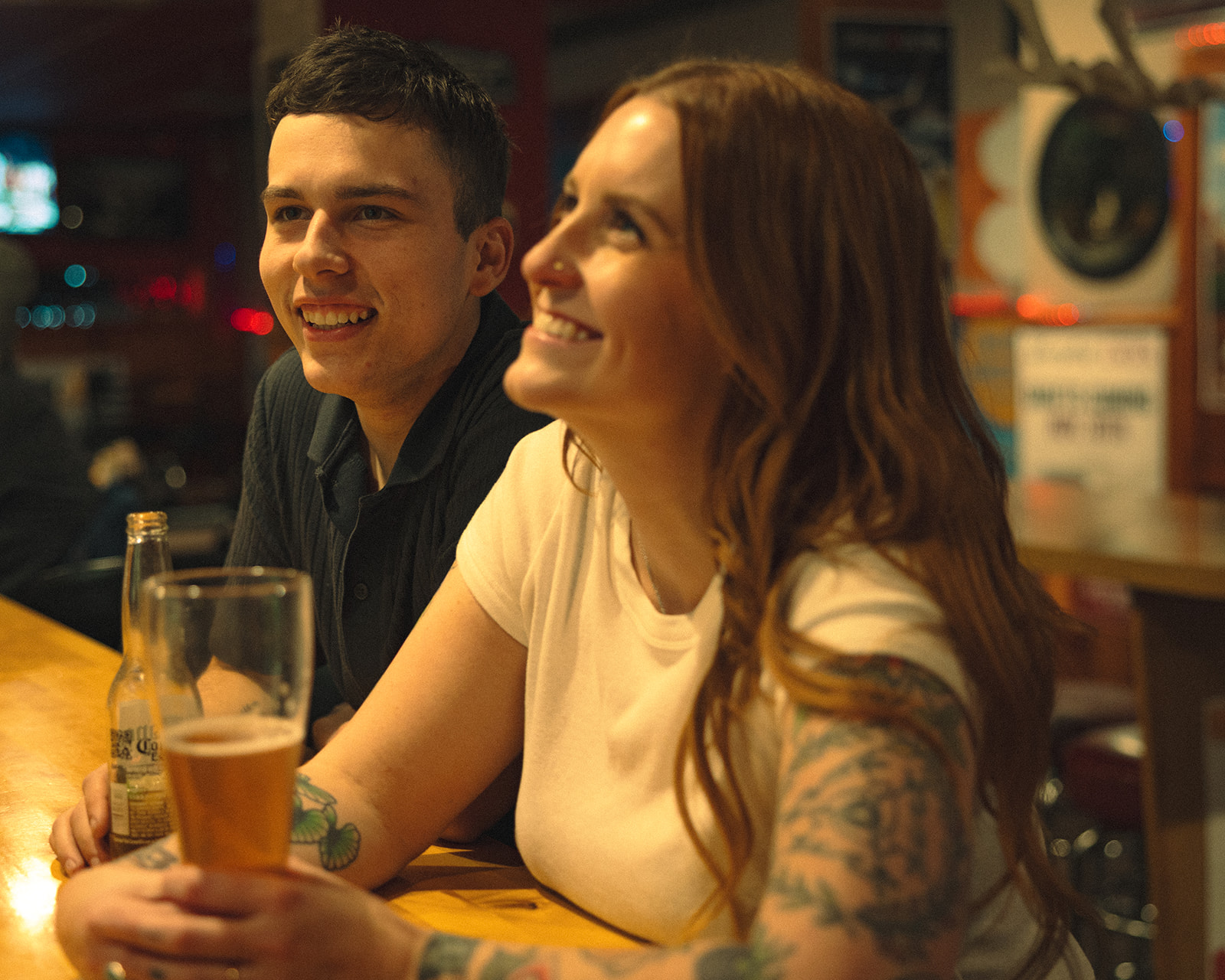 Candid photo of a couple smiling at the bar while having drinks together for dive bar engagement photos.