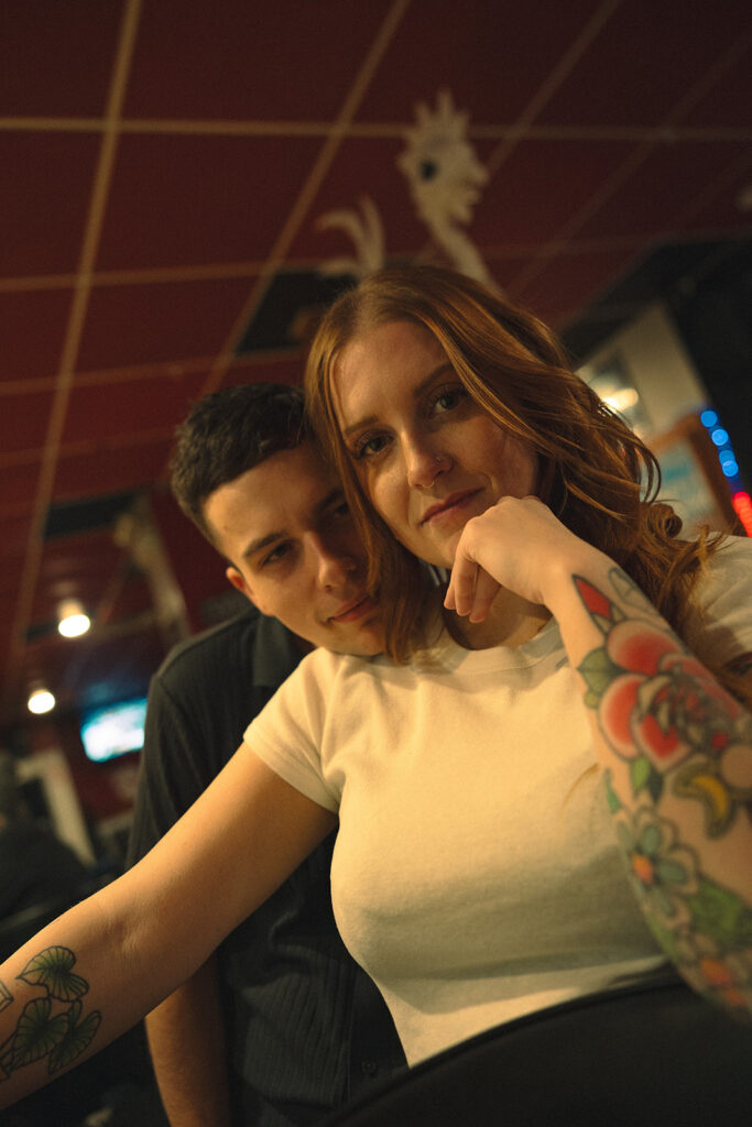 Couple sitting at a bar having drinks together and looking into the camera.