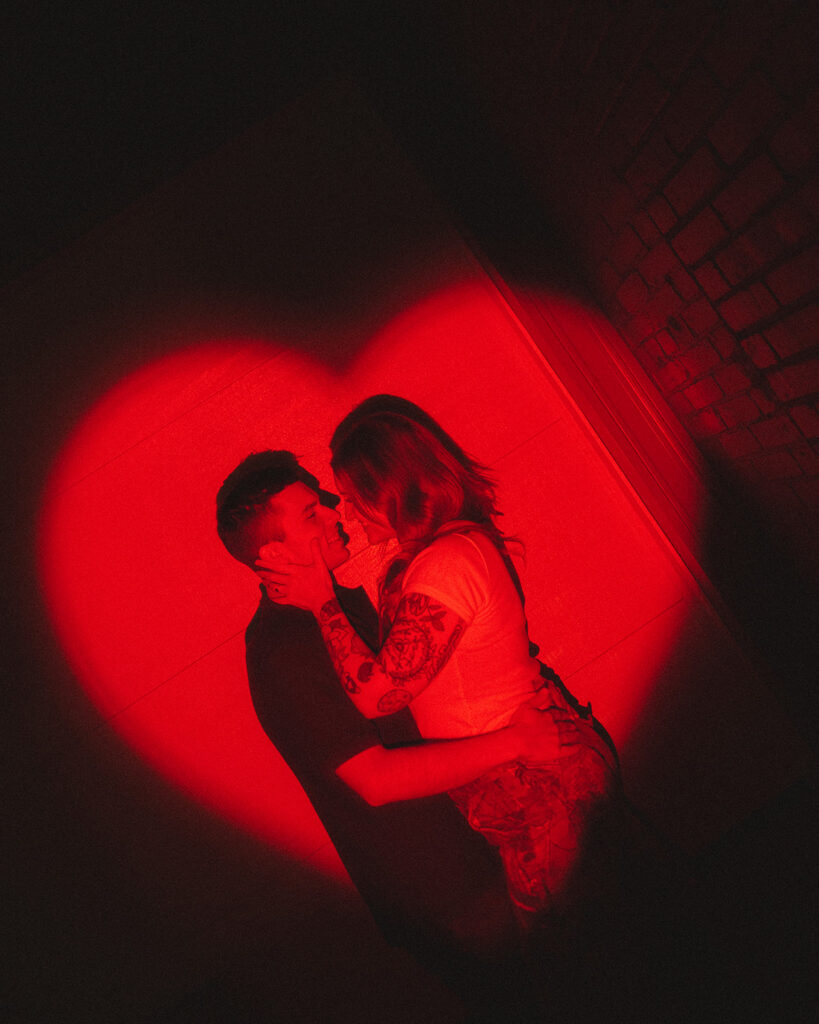 Couple posing inside of a red heart shadow effect during their dive-bar engagement photos in Michigan.