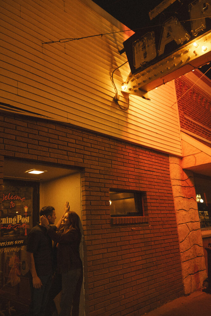 Woman caressing her fiances face during their Michigan engagement photos outside of The Evening Post Bar & Grill in Clare.