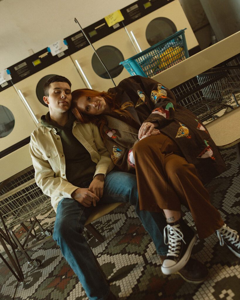 Couple posing inside of a laundromat for their vintage-inspired Michigan engagement photos.