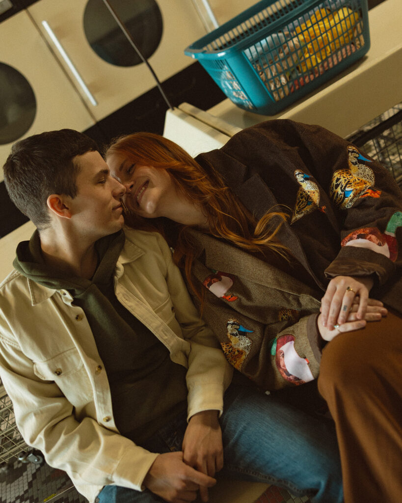 Candid photo of a couple sitting and smiling together at a laundromat for their Michigan engagement photos.