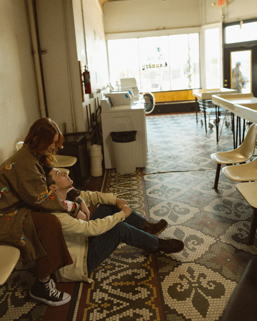 Couple sitting together at a Michigan laundromat for their vintage-inspired engagement photos.