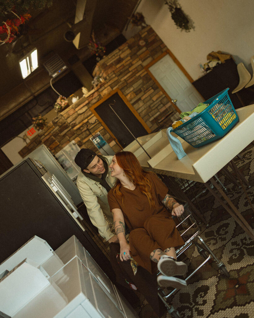 Man pushing his fiancé in a laundromat basket.