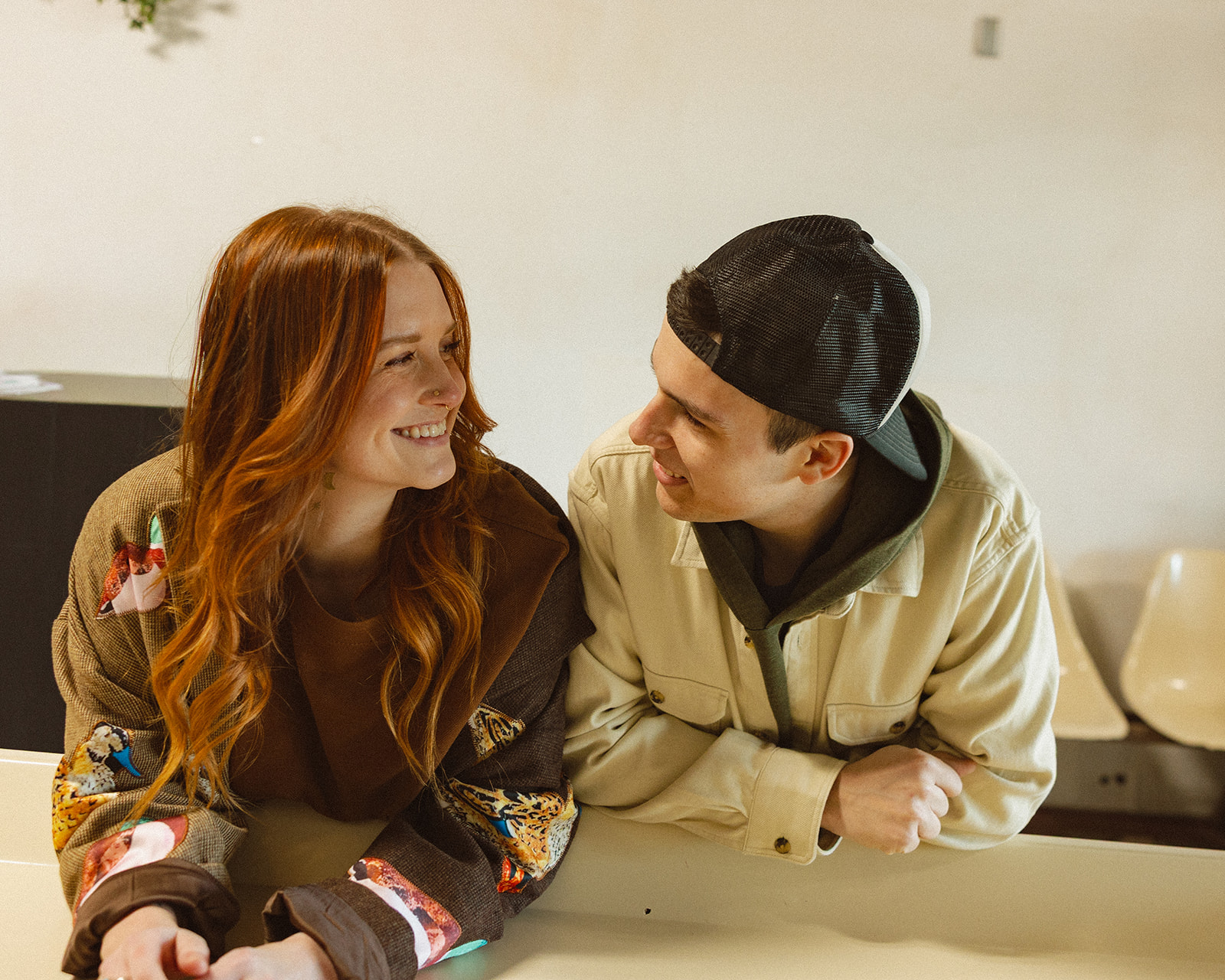 Couple smiling and leaning against a laundromat table for their engagement session.