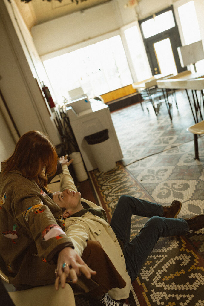 Couple sitting together at a Michigan laundromat for their vintage-inspired engagement photos.