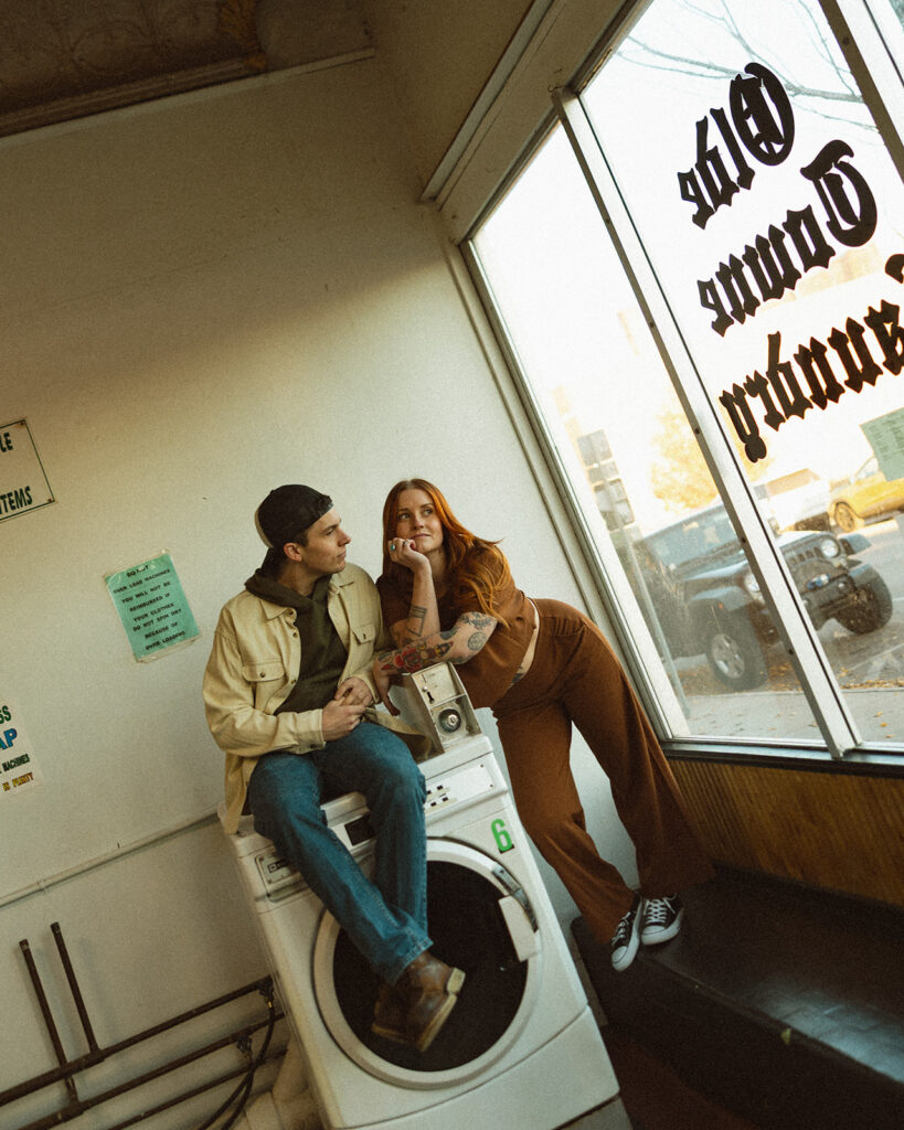 Couple posing against a washing machine for their laundromat photoshoot in Michigan.