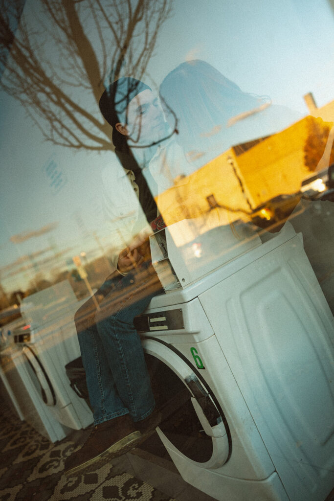 Photo of a couple through the window as they sit with a washing machine.
