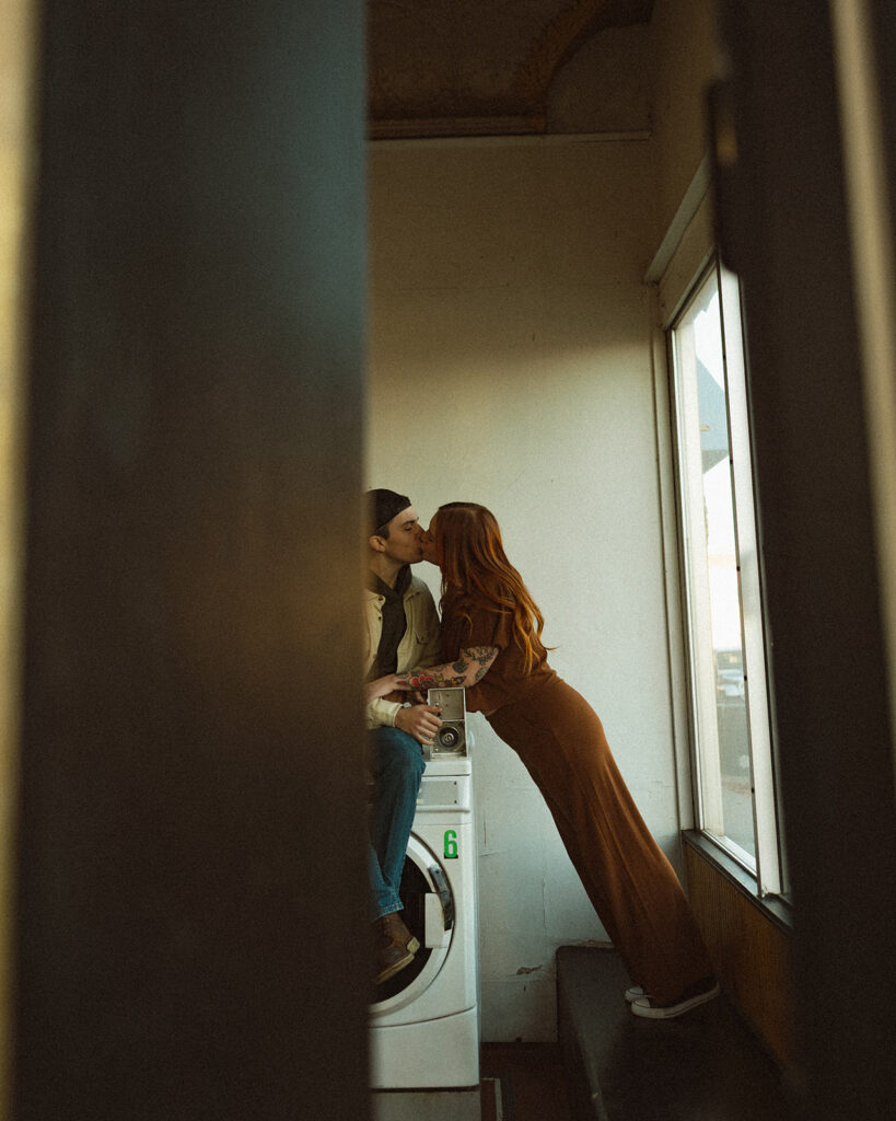 Documentary style photo of a couple kissing at a local laundromat during their engagement session.