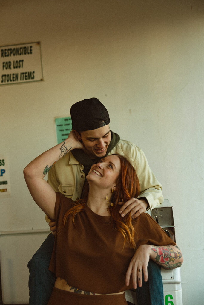 Couple smiling at one another during their Michigan laundromat photoshoot.