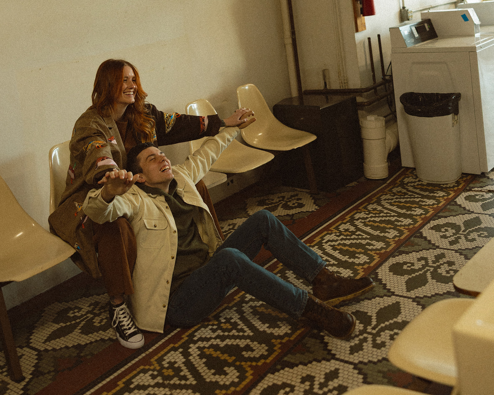 Couple sitting together at a Michigan laundromat for their vintage-inspired engagement photos.