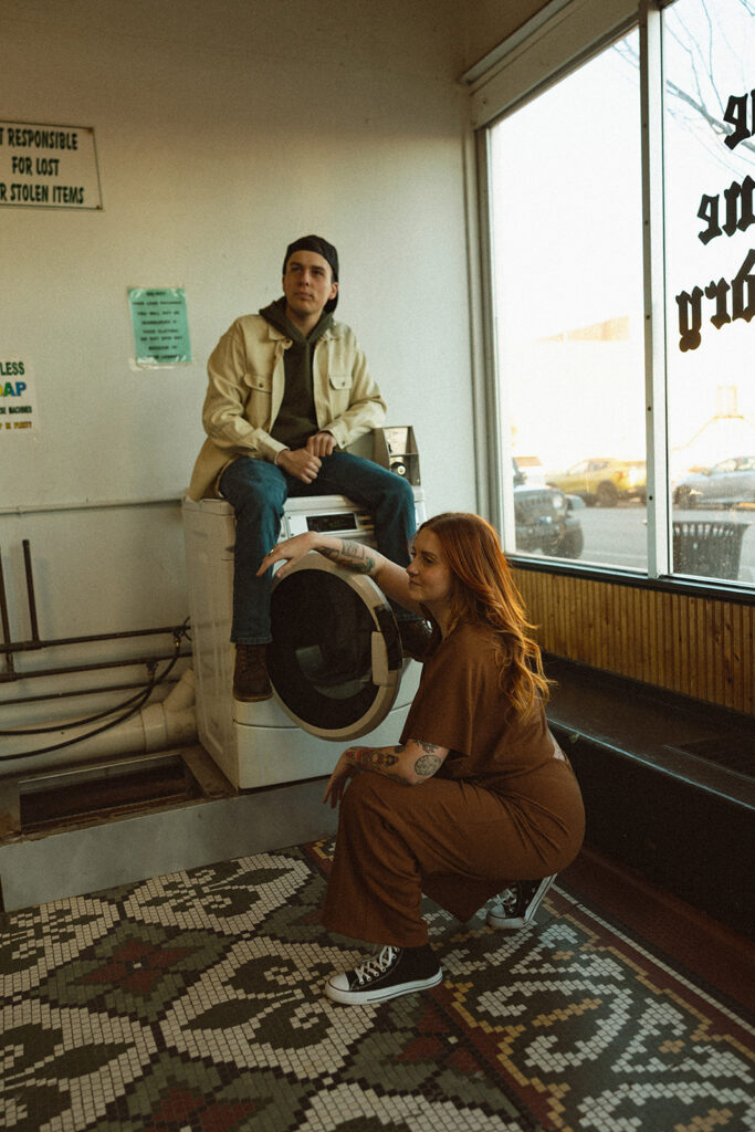Editorial style photos of a couple posing with a washing machine during their laundromat photoshoot in Michigan.