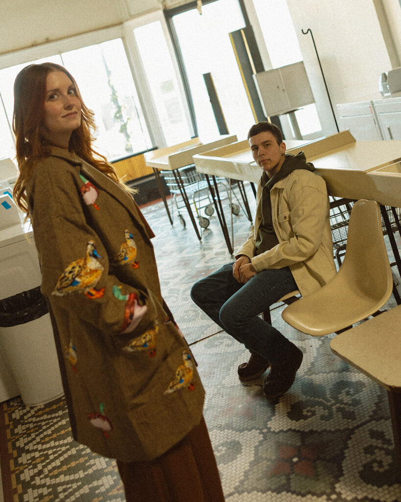 Couple posing inside of a laundromat for their vintage-inspired Michigan engagement photos.