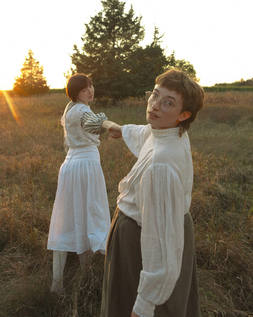 Couple holding hands in a rural field during their Midwestern Gothic engagement photos.
