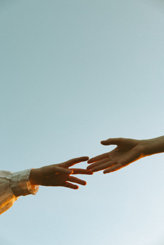 Couple hands reaching out for each other with the sky showing above during their Michigan engagement photos.