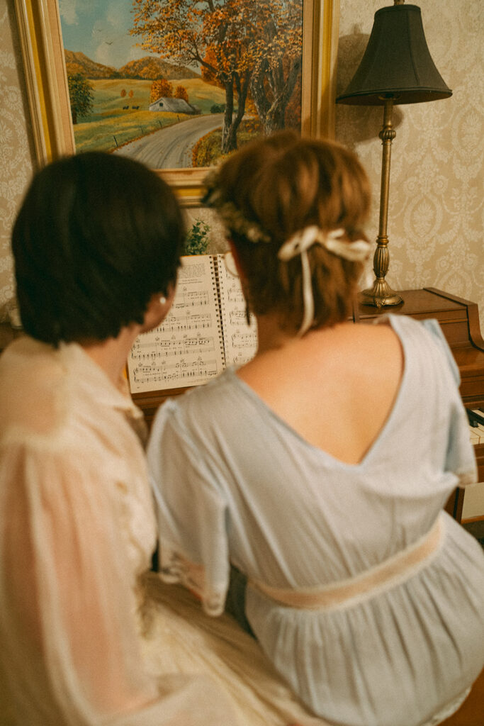 Couple sitting beside each other at a piano and looking at sheet music inside a vintage farmhouse.