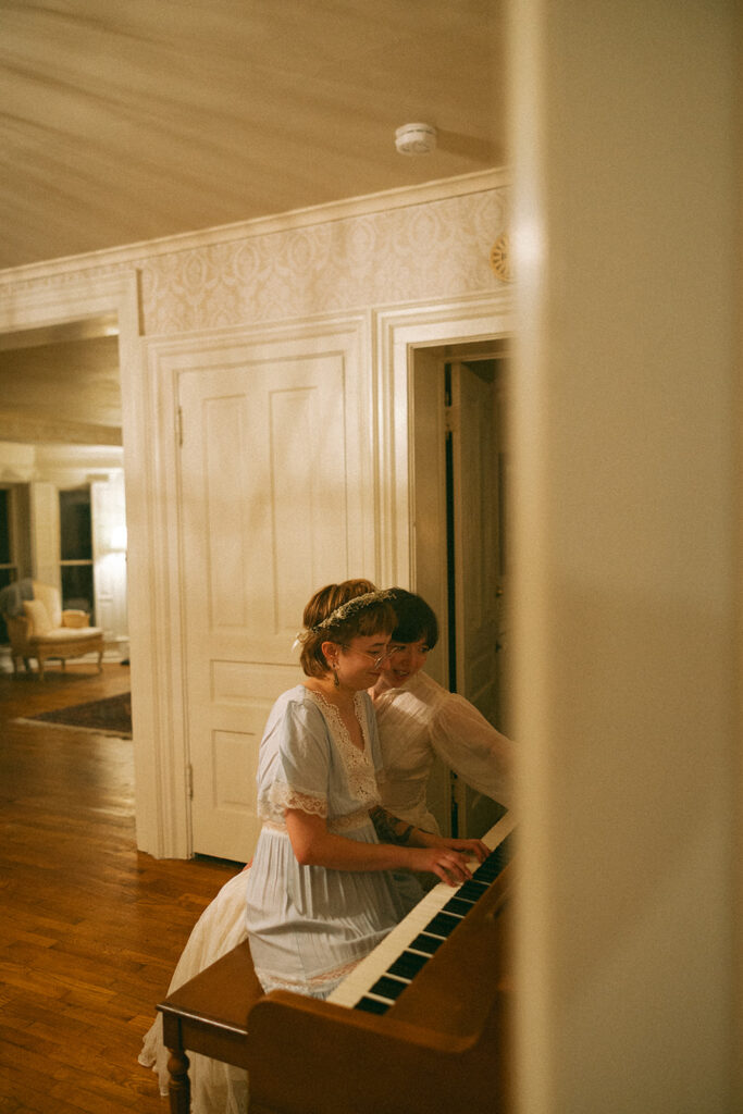 Couple sitting beside each other at a piano and looking at sheet music inside a vintage farmhouse.