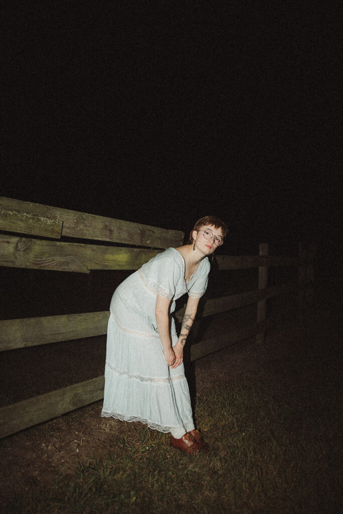 Person leaning against a fence in a vintage dress for her unique Michigan engagement photos.