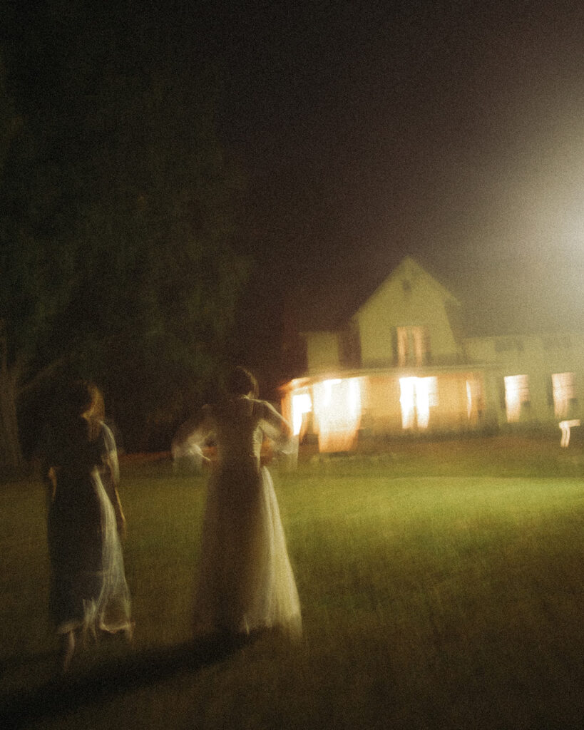 Blurred nighttime view of a couple walking towards a vintage farmhouse.