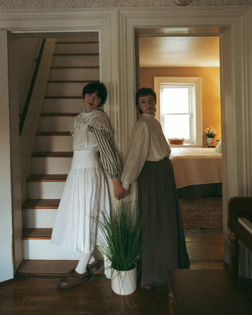 Couple holding hands between two doorways inside an old Michigan farmhouse.