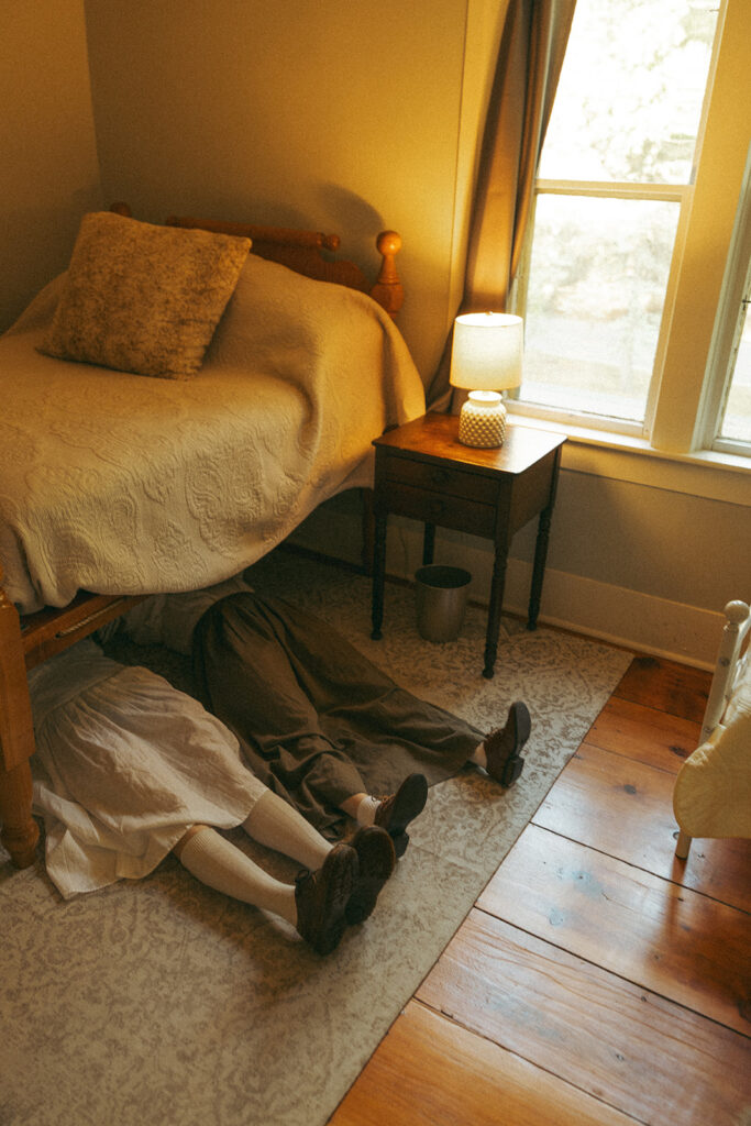 Couple lying beneath a bed during their playful, unconventional engagement session.