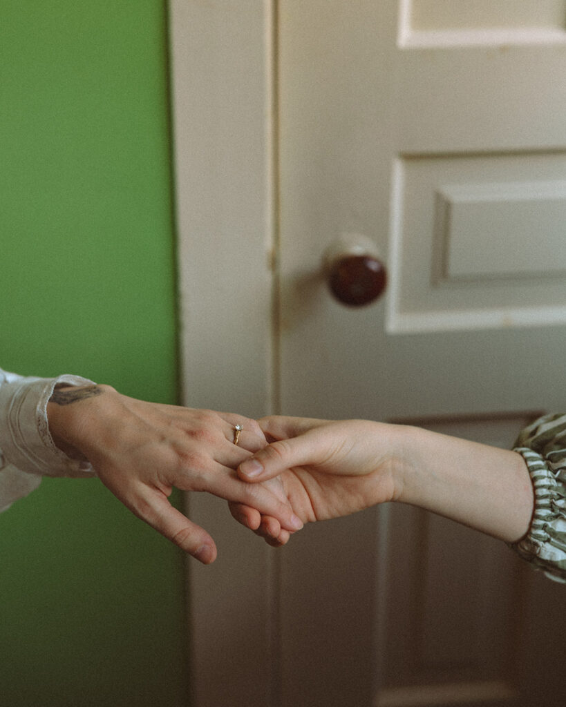 Close-up of a couple holding hands with an engagement ring visible inside a vintage farmhouse.