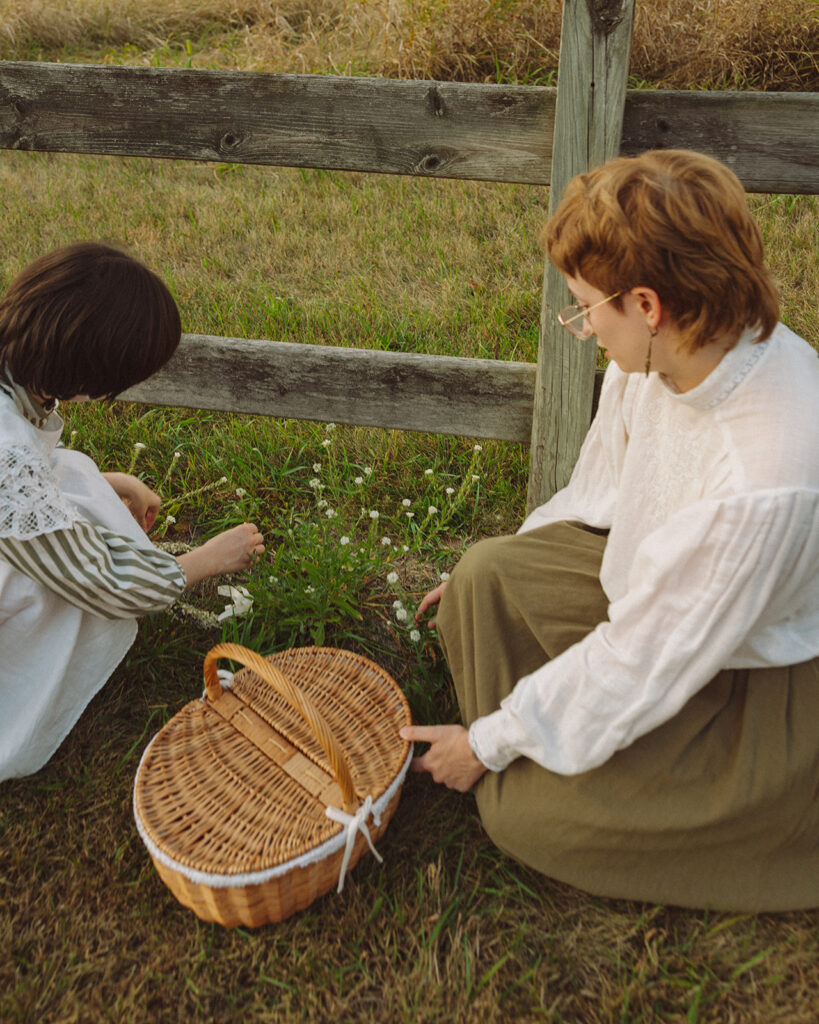 Couple gathering small flowers beside a wooden fence during their Michigan engagement session.