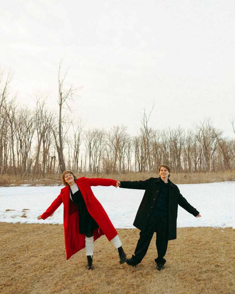 Couple playfully balancing while holding hands beside a snow-covered field.