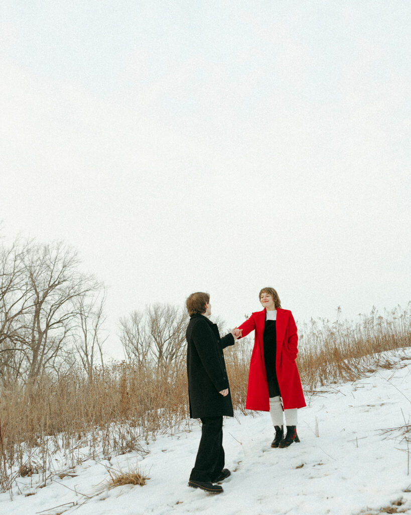 Couple holding hands on a snowy trail during their winter engagement session.