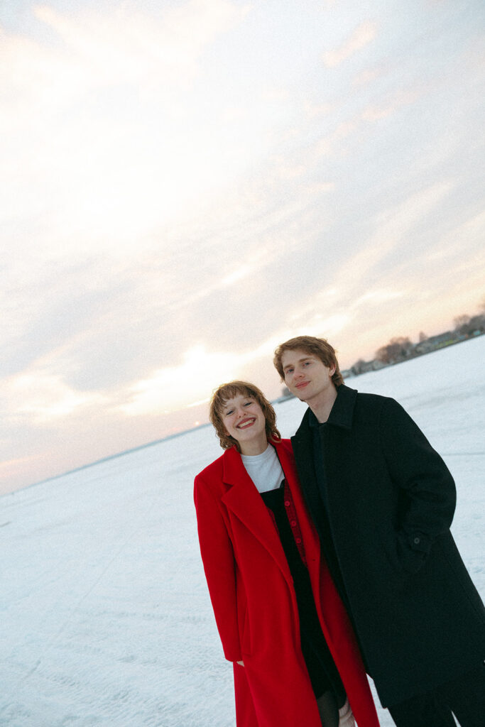 Couple smiling at the camera as they pose for their outdoor Detroit winter engagement photos at Lake St. Clair Metropark.