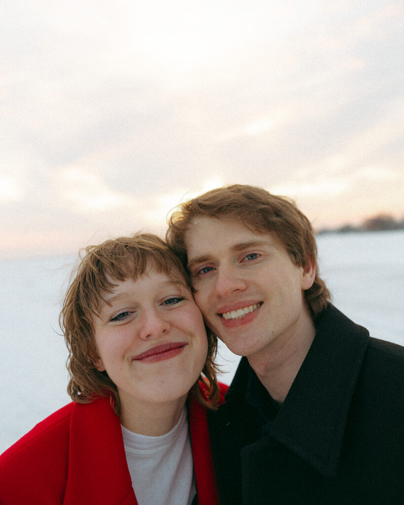 Couple smiling at the camera as they pose for their outdoor Detroit winter engagement photos at Lake St. Clair Metropark.