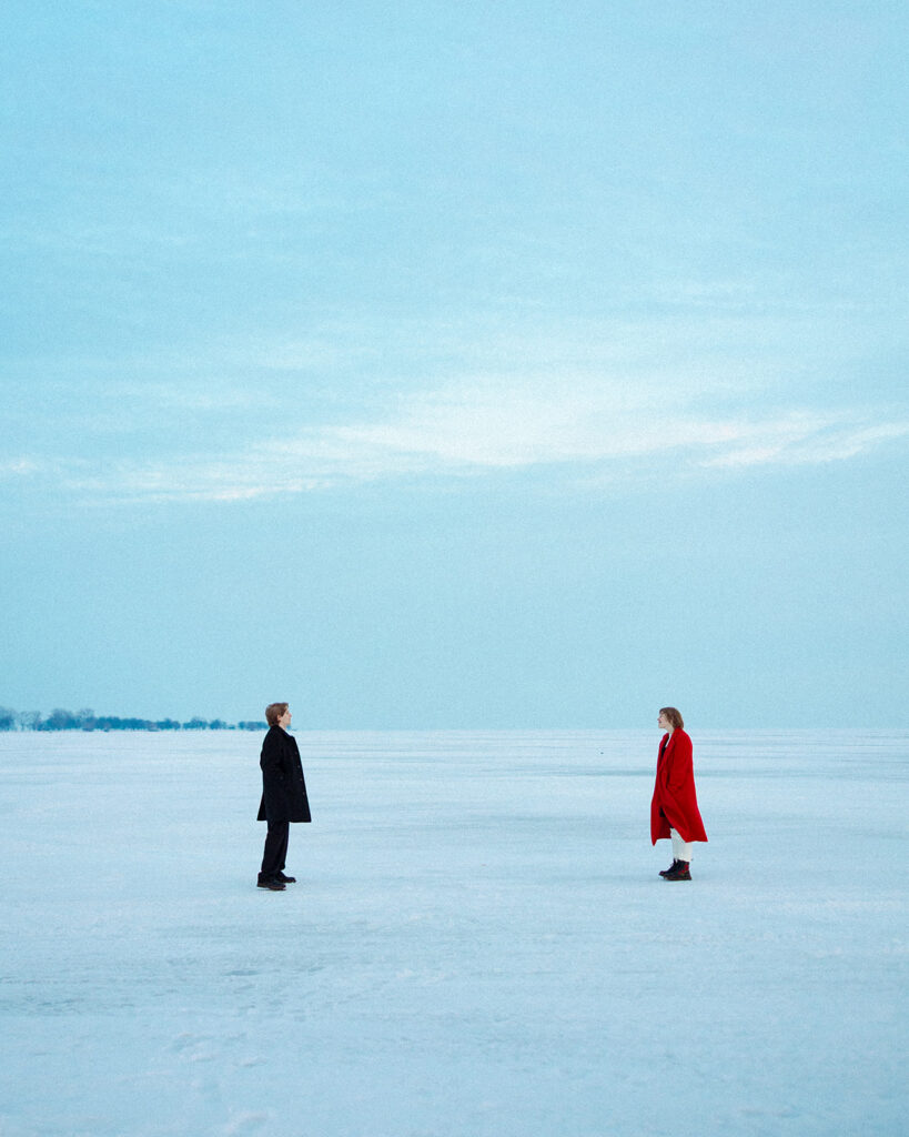 Couple standing apart on the frozen lake during their Lake St. Clair Metropark engagement photos.