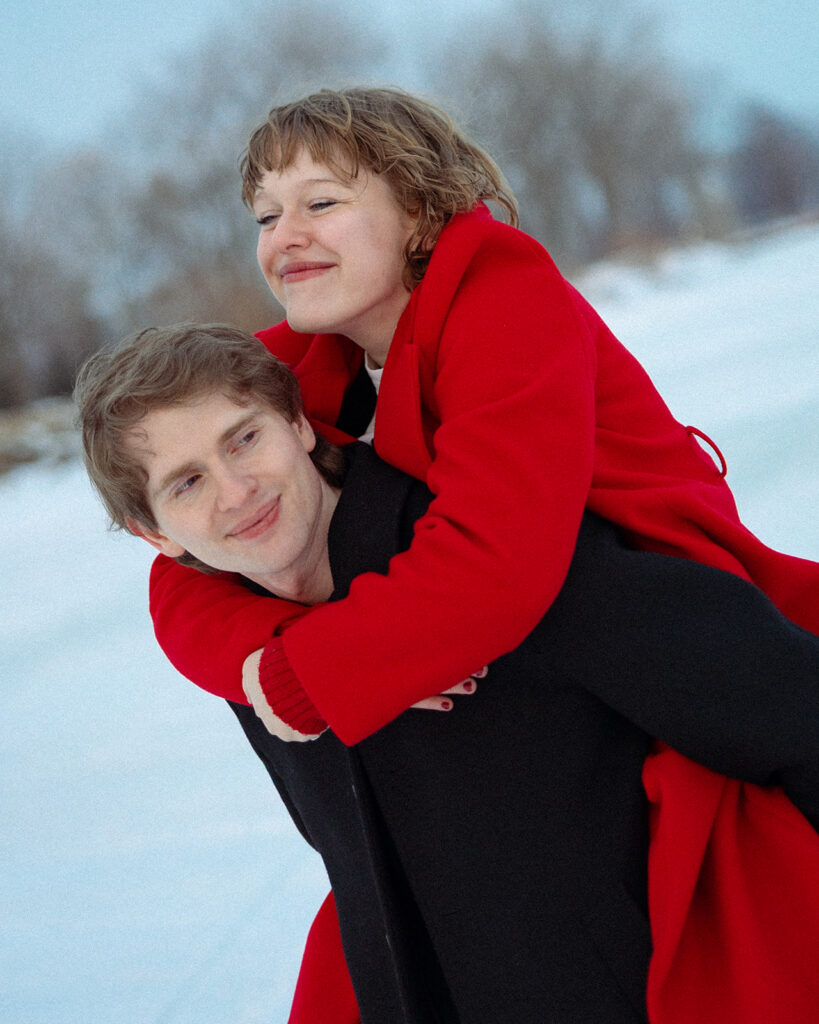 Man giving his fiancé a piggy back ride during their outdoor Detroit winter engagement photos at St. Clair Metropark.