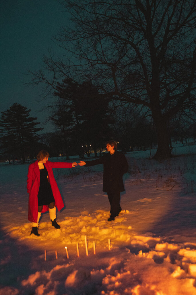 Couple holding hands in the snow with candles at Lake St. Clair Metropark.