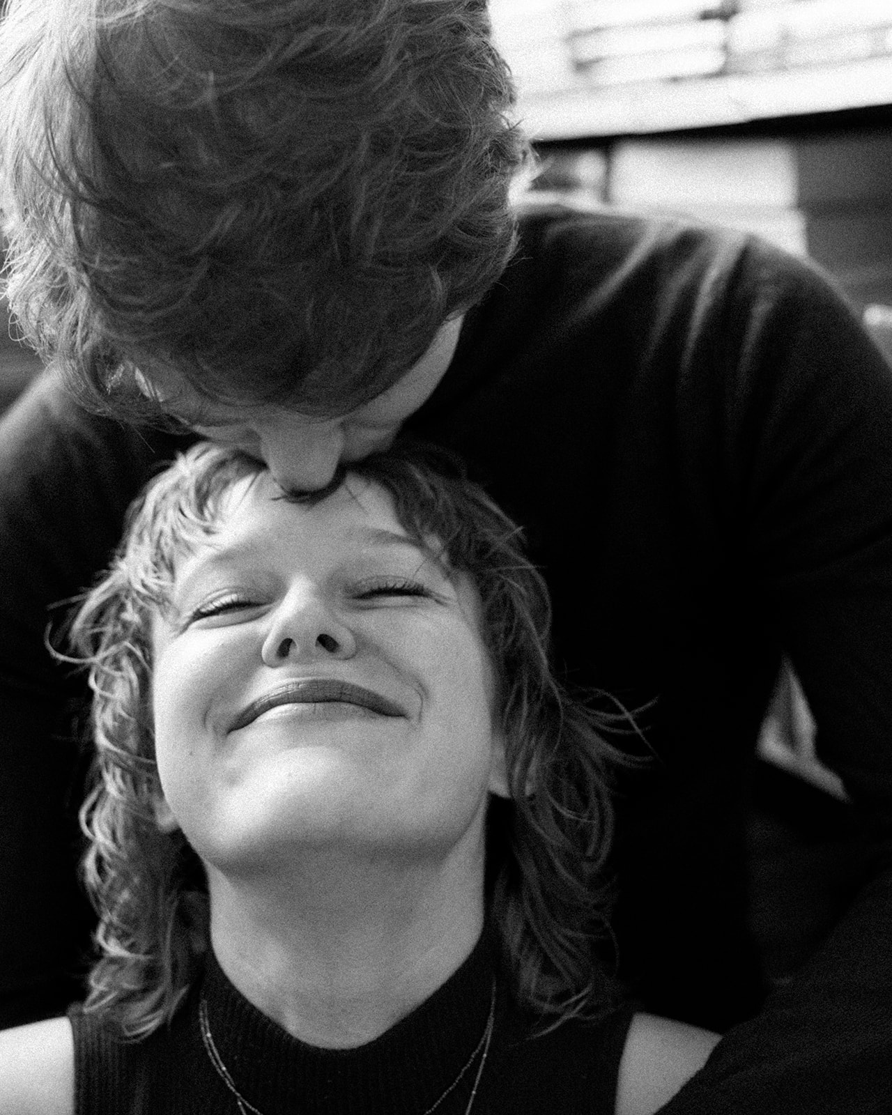 Black and white photo of a man kissing his fiancés forehead during their indoor Detroit winter engagement photos.