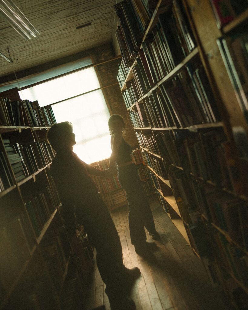 Moody silhouette of a couple walking together at the end of a bookstore aisle.