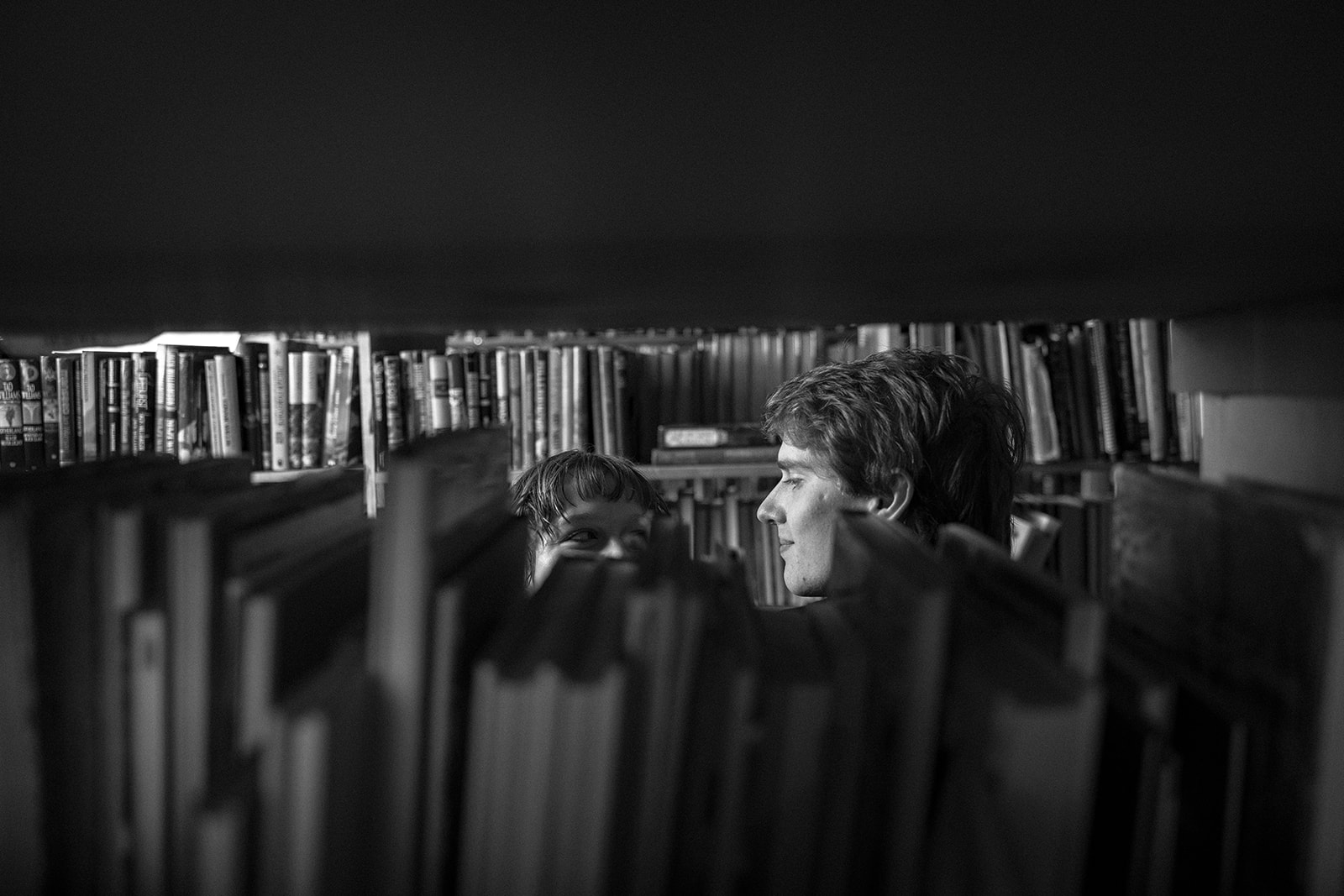 Black-and-white photo of a couple looking at each other over rows of books.