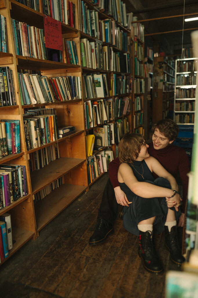 Couple sitting between tall bookshelves during their Detroit winter engagement photos.