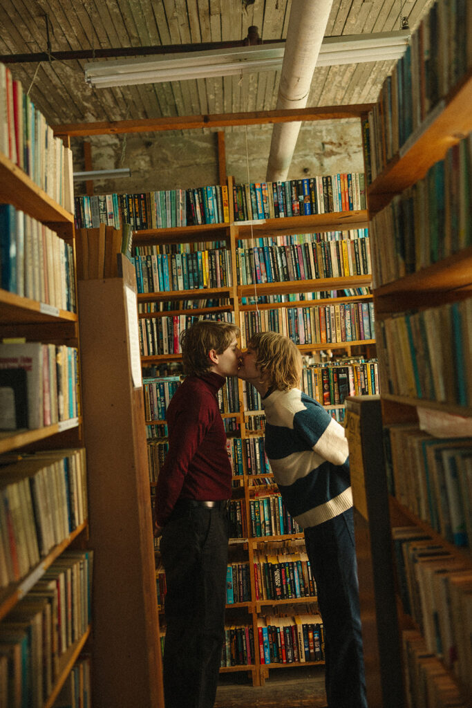 Couple kissing between tall bookshelves during their Detroit winter engagement photos.