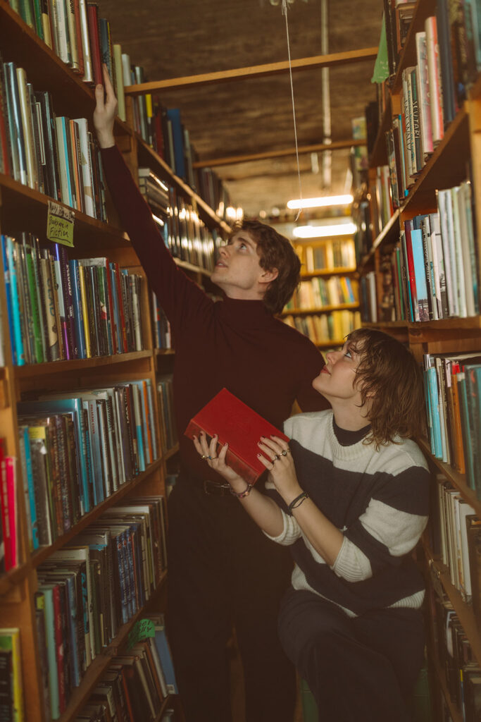 Couple browsing colorful books together during their Detroit bookstore engagement photos.