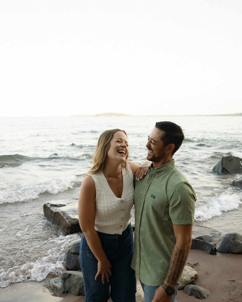 Couple laughing for their Michigan beach engagement photos in Marquette on Little Presque Isle.
