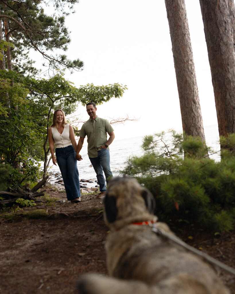 Couple walking toward their dog on a wooded trail overlooking Lake Superior at Little Presque Isle.