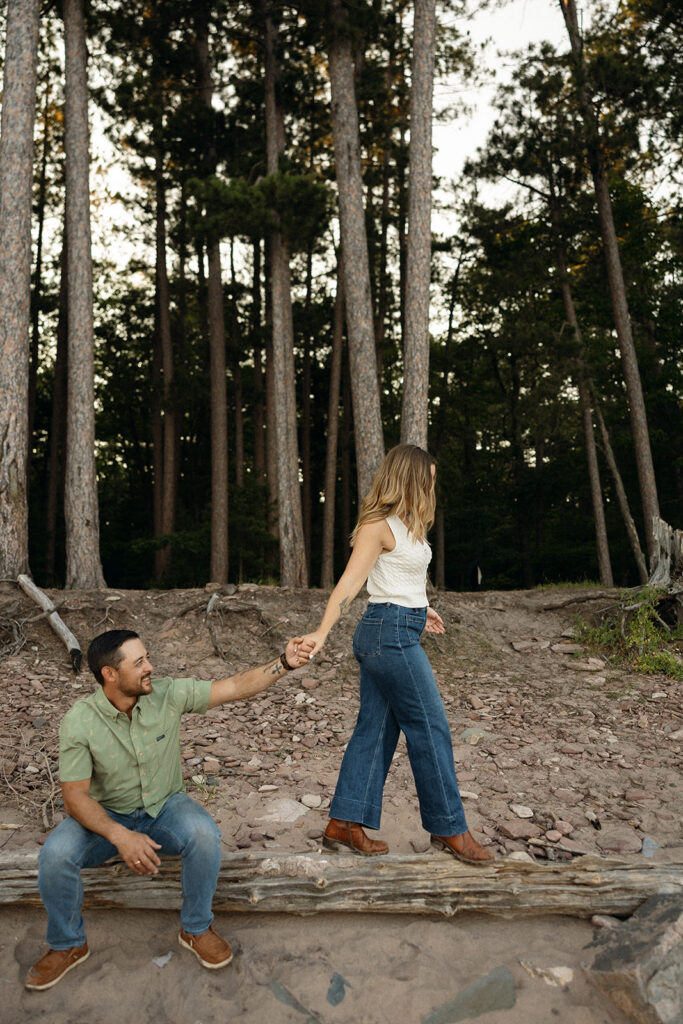 Couple holding hands beside driftwood and tall pine trees at Little Presque Isle.