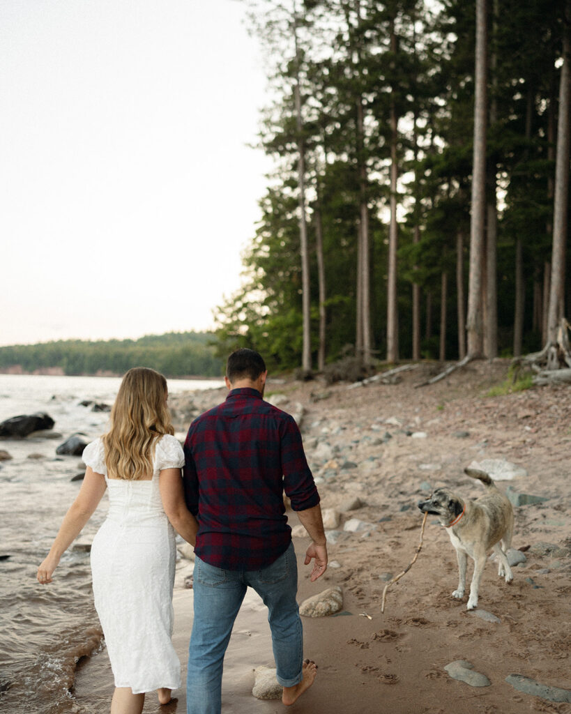 Couple walking together along the beach with their dog during their engagement session at Little Presque Isle.