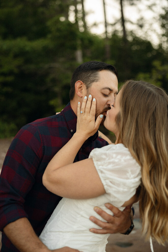 Couple laughing as one lifts the other along the beach during their Little Presque Isle engagement photos.